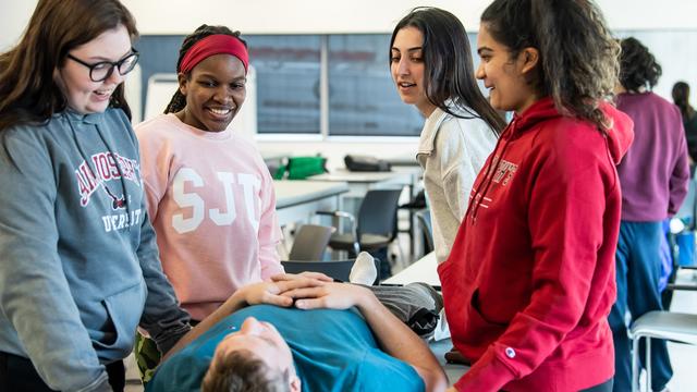 Four students standing over a patient in a physical therapy setting