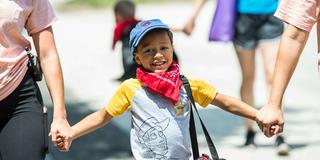 little boy holding the hands of adults while walking
