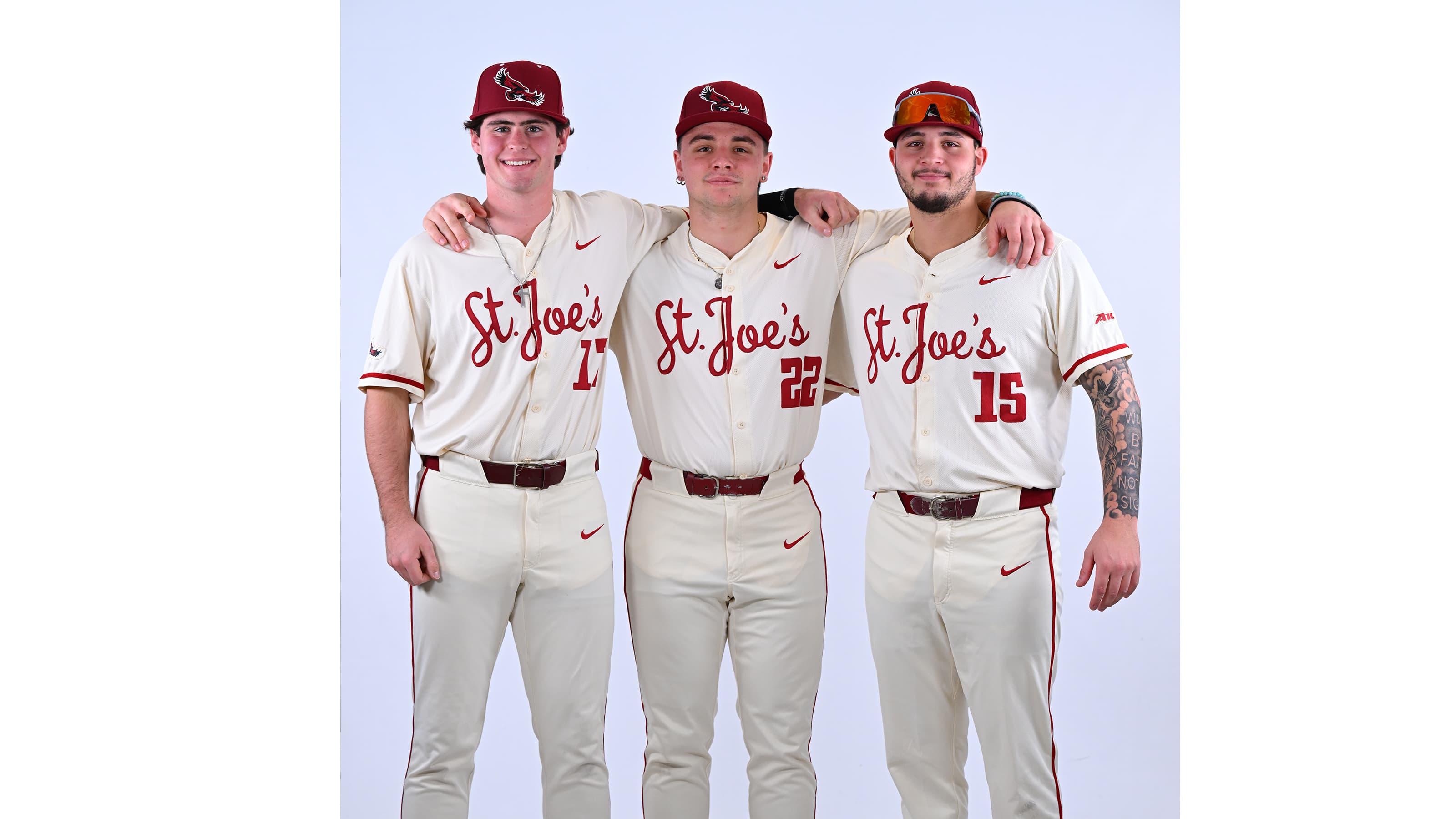 Three male baseball players standing next to each other wearing St. Joe's uniform