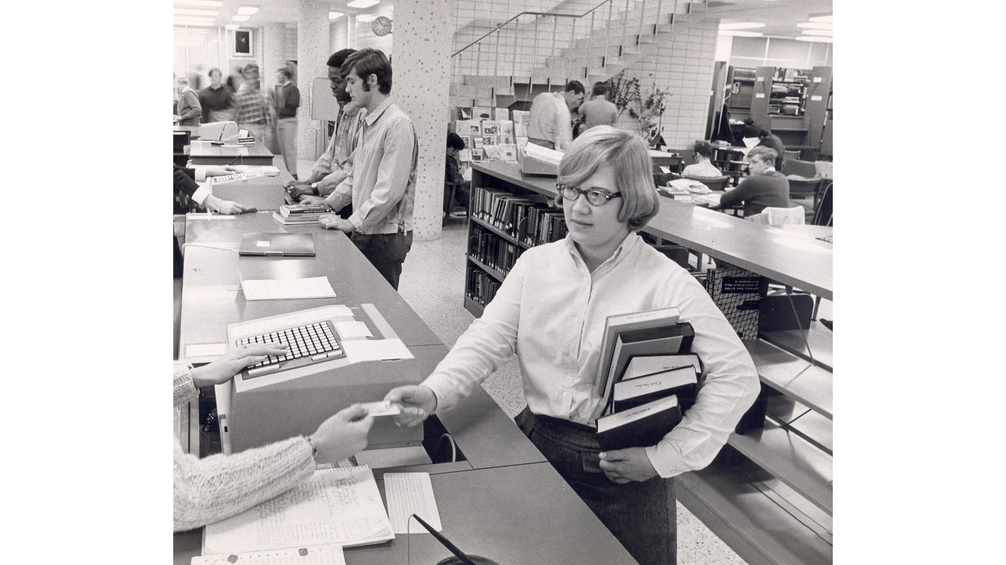 Black and white photo of female student checking out book in library