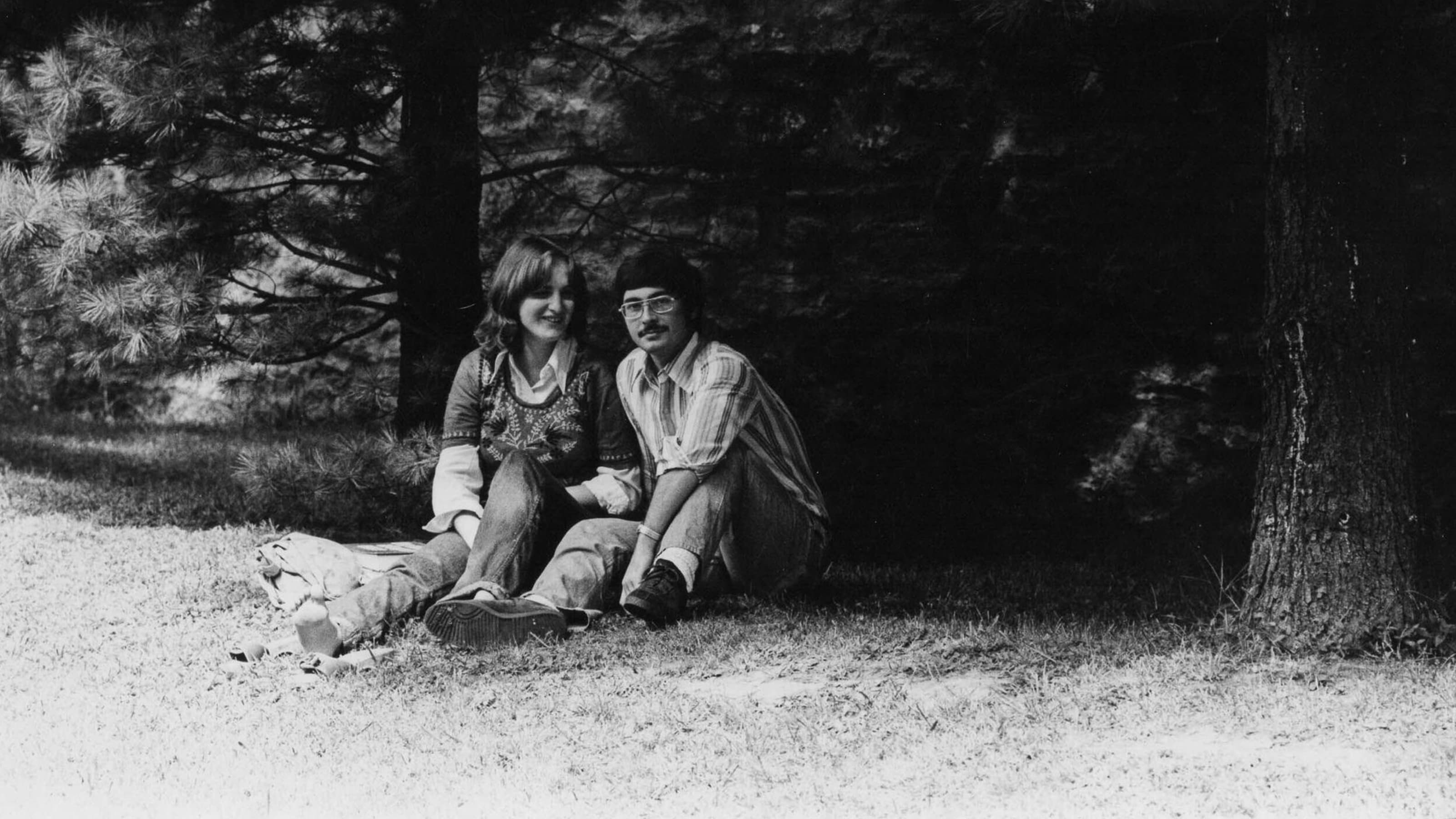 Two students sitting on the lawn under pine trees on Hawk Hill