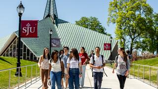 A group of smiling students walks on Hawk Hill