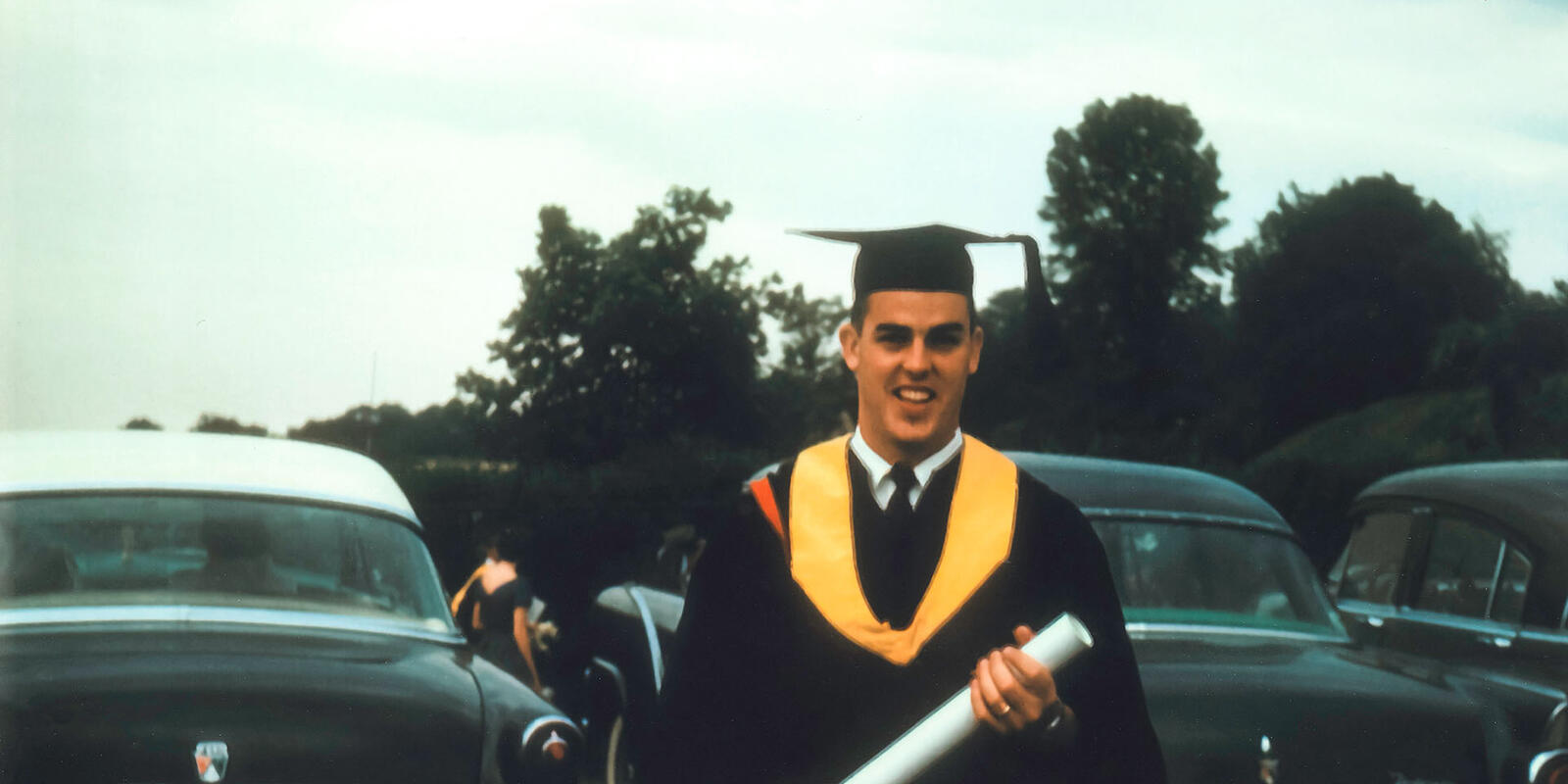 A man in graduation regalia holding a rolled up piece of paper