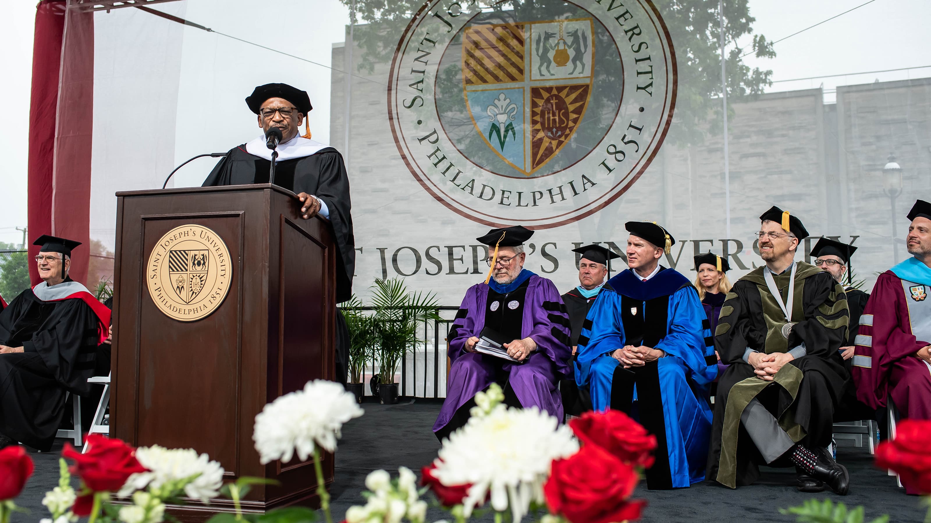 Speaker at podium at Commencement ceremony with faculty seated to the right