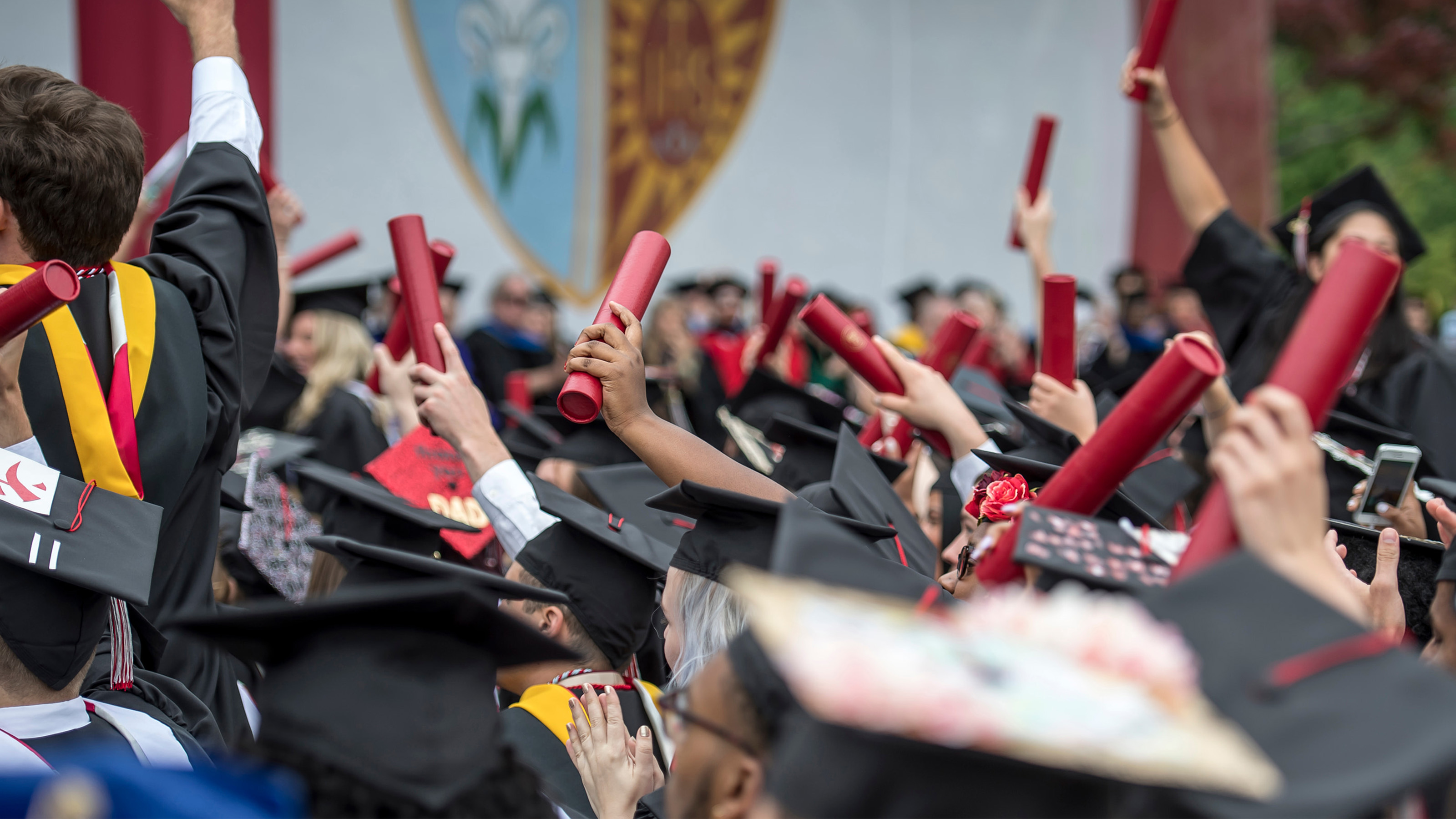 Students in black caps and gowns holding their red diploma scrolls in the air