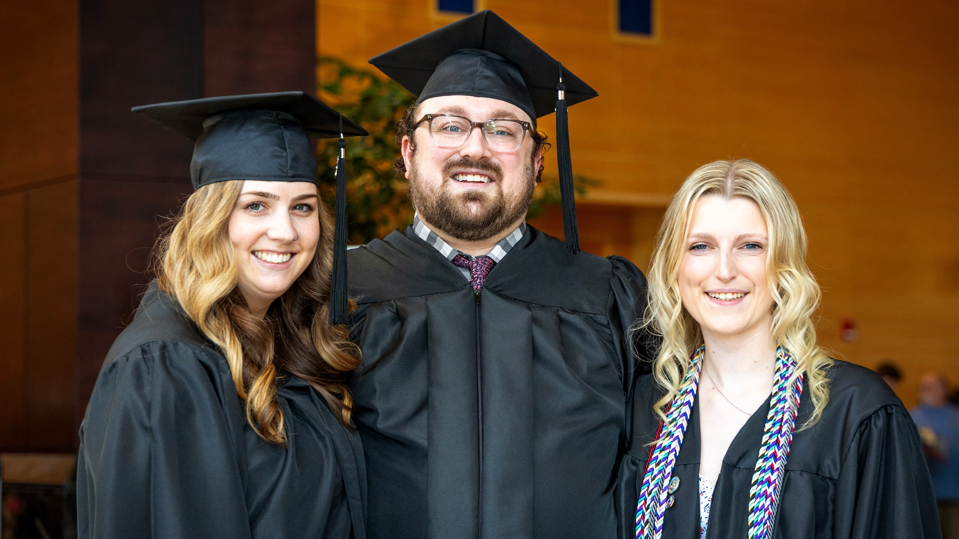 Three graduates in black regalia standing shoulder to shoulder