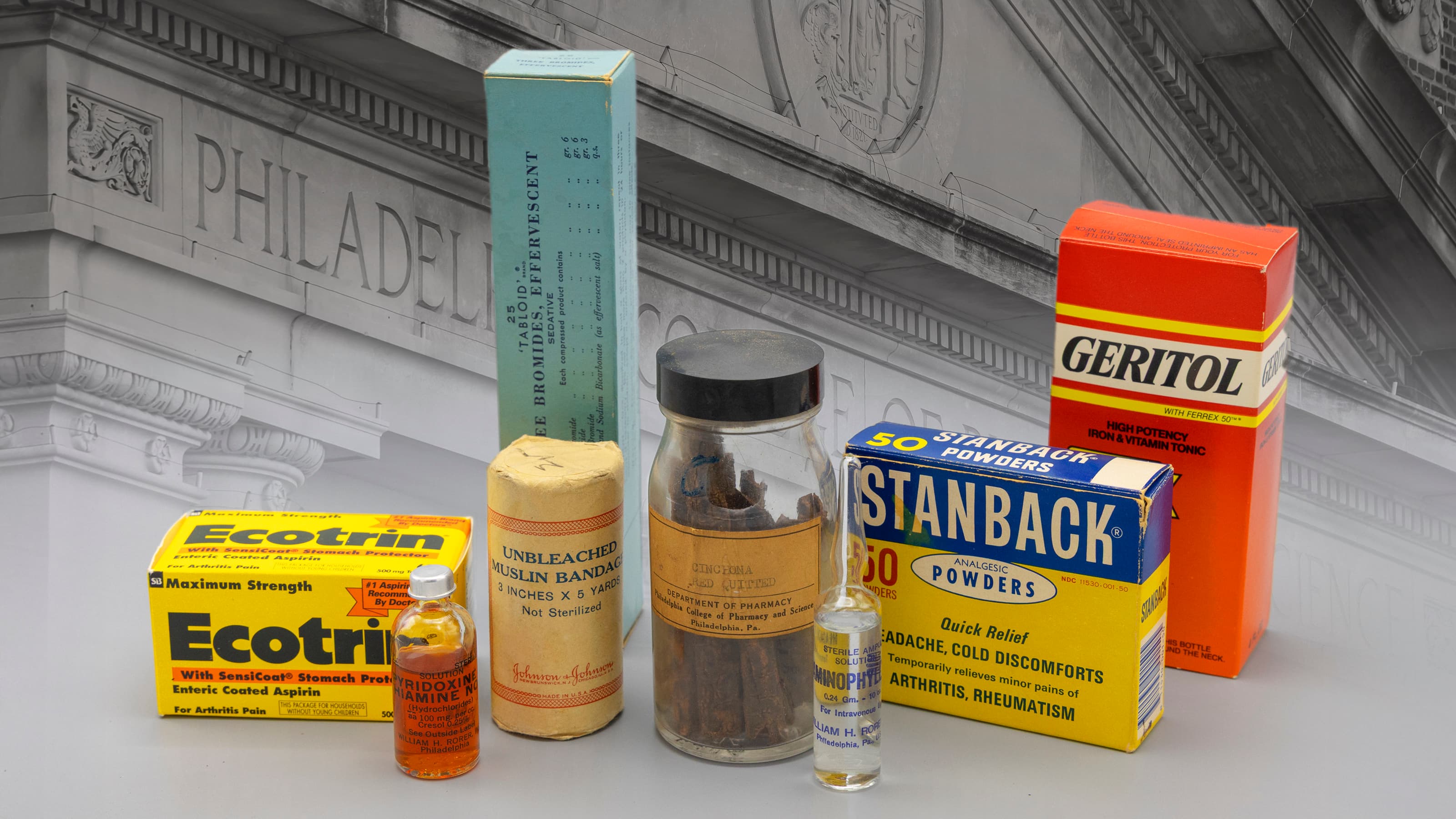 Group of pharmacy artifacts lined up with Philadelphia College of Pharmacy building behind it