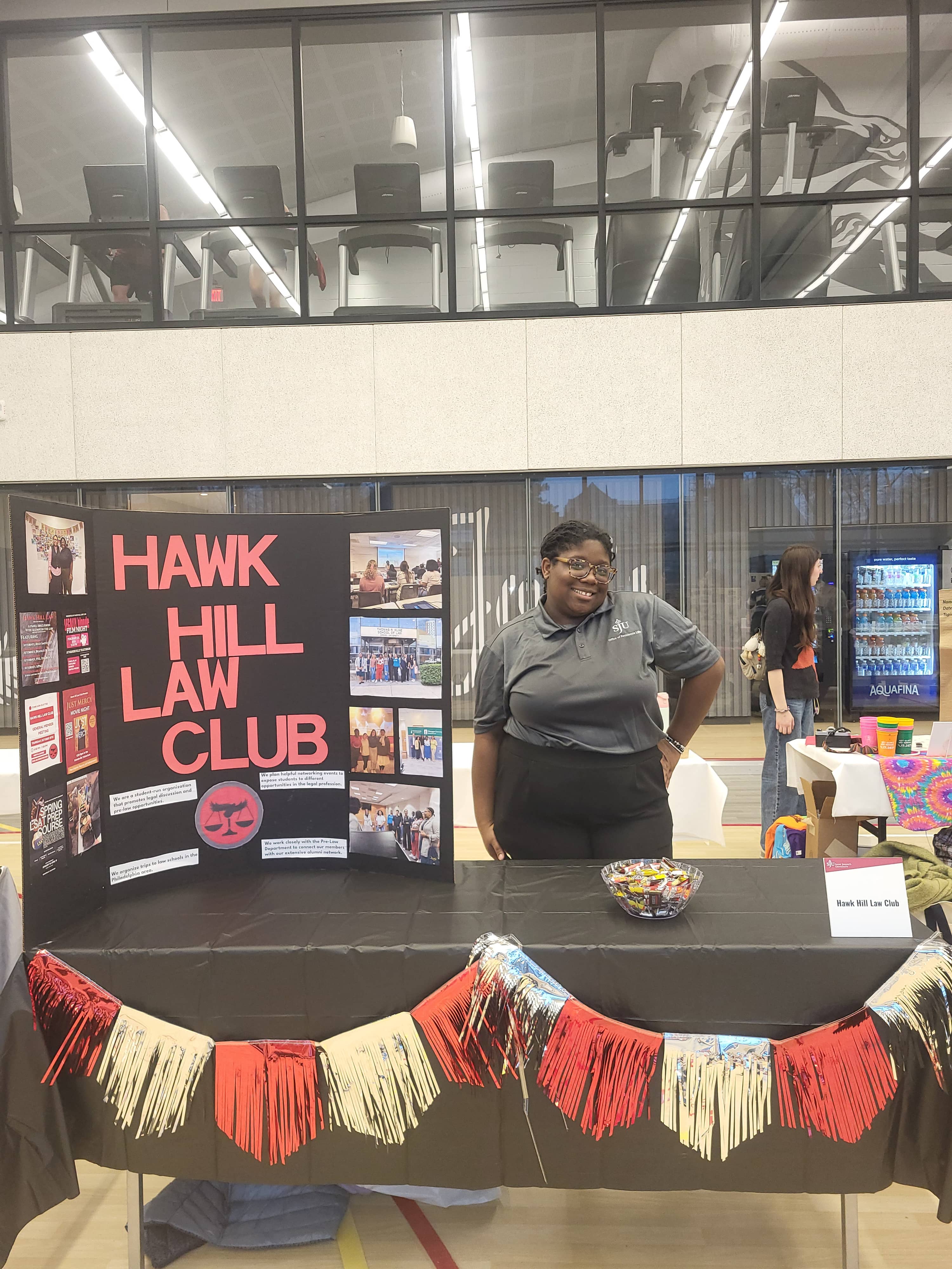 Faith Adedokun standing next to Hawk Hill Law Club poster