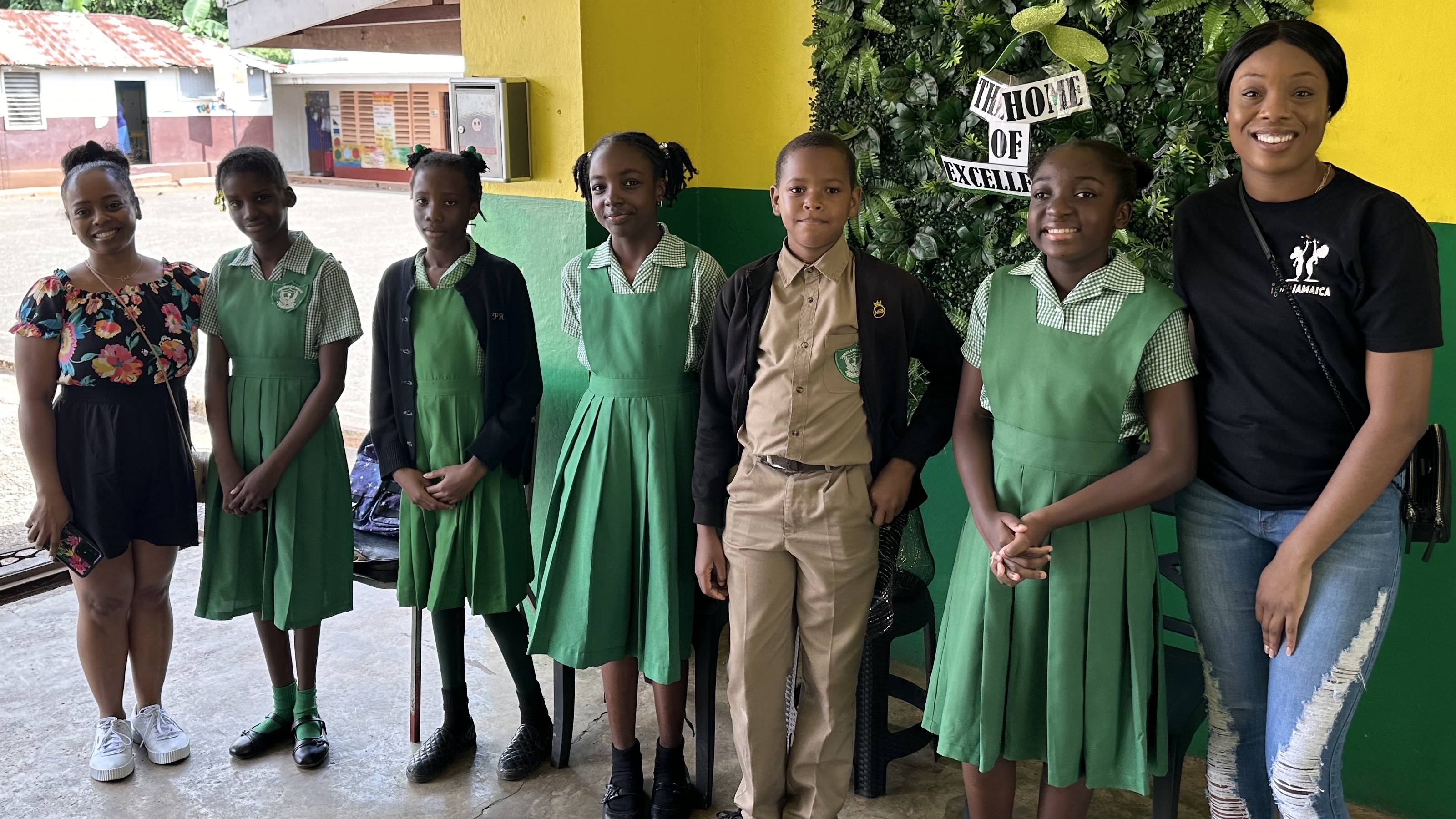 Kimisha Simpson, MS ’16, EdD ’25, stands next to five children in green uniforms.
