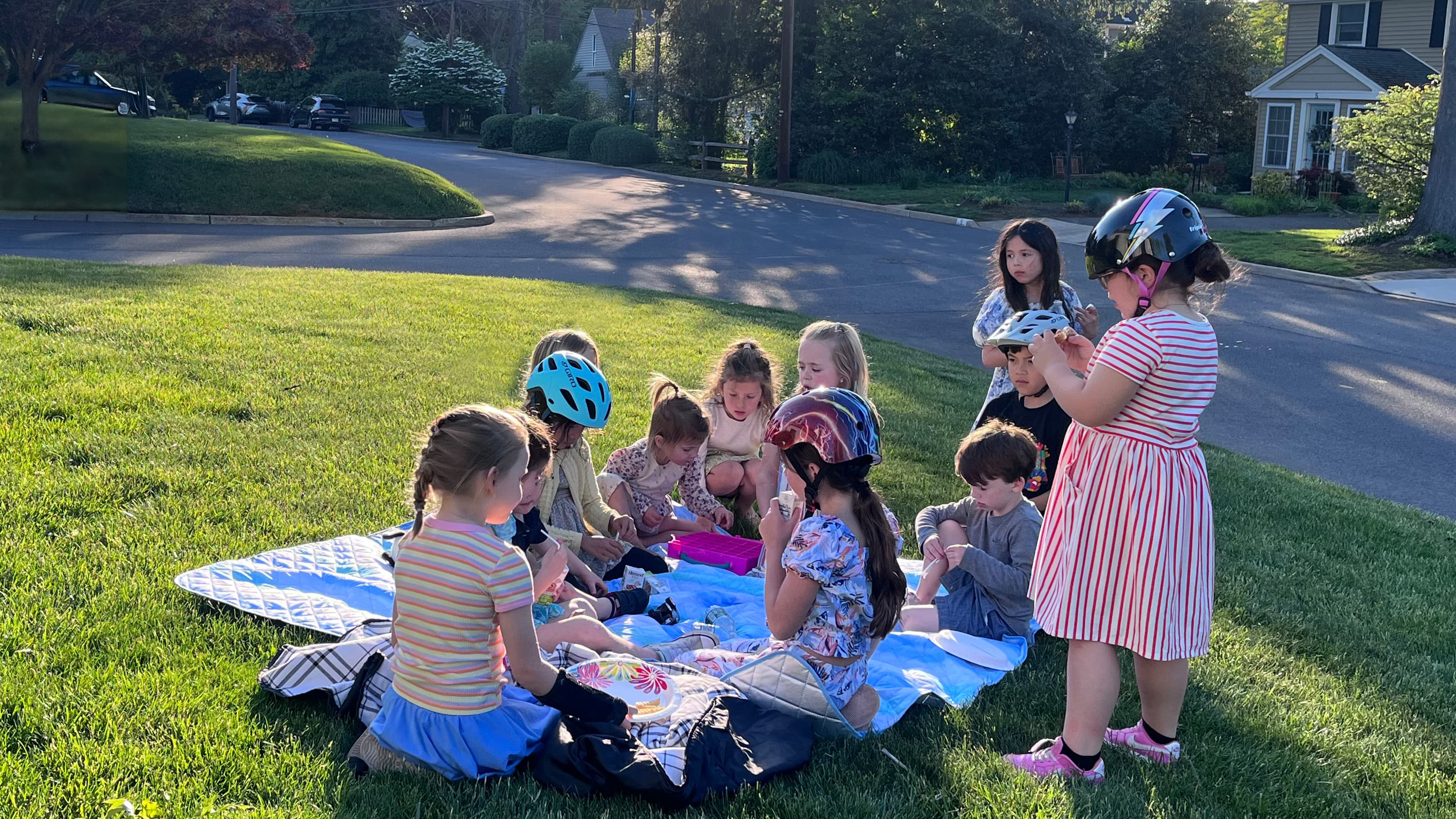 Kids gathered together on a picnic blanket with on a front lawn