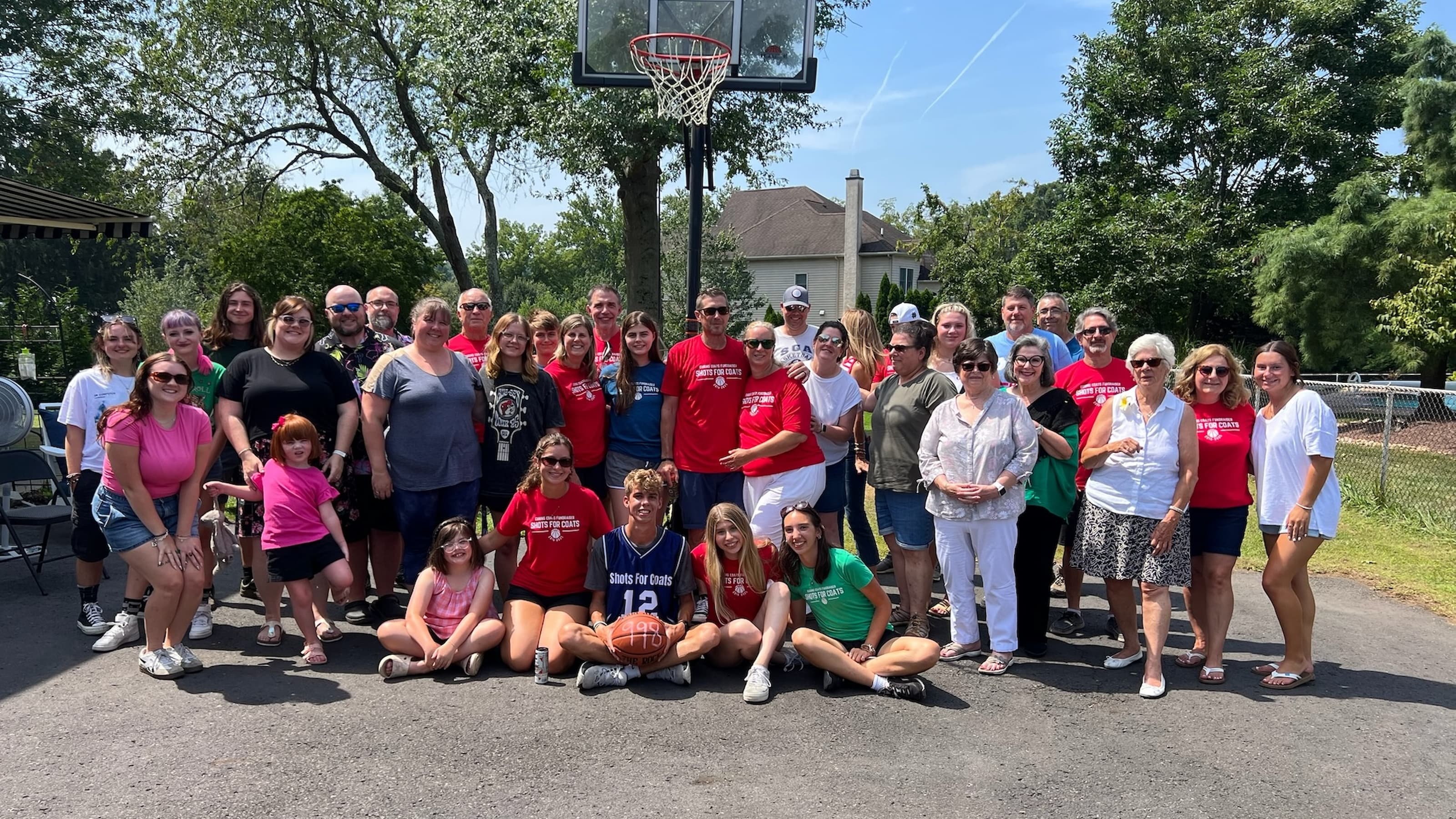 A group of smiling people in front of a driveway basketball net.