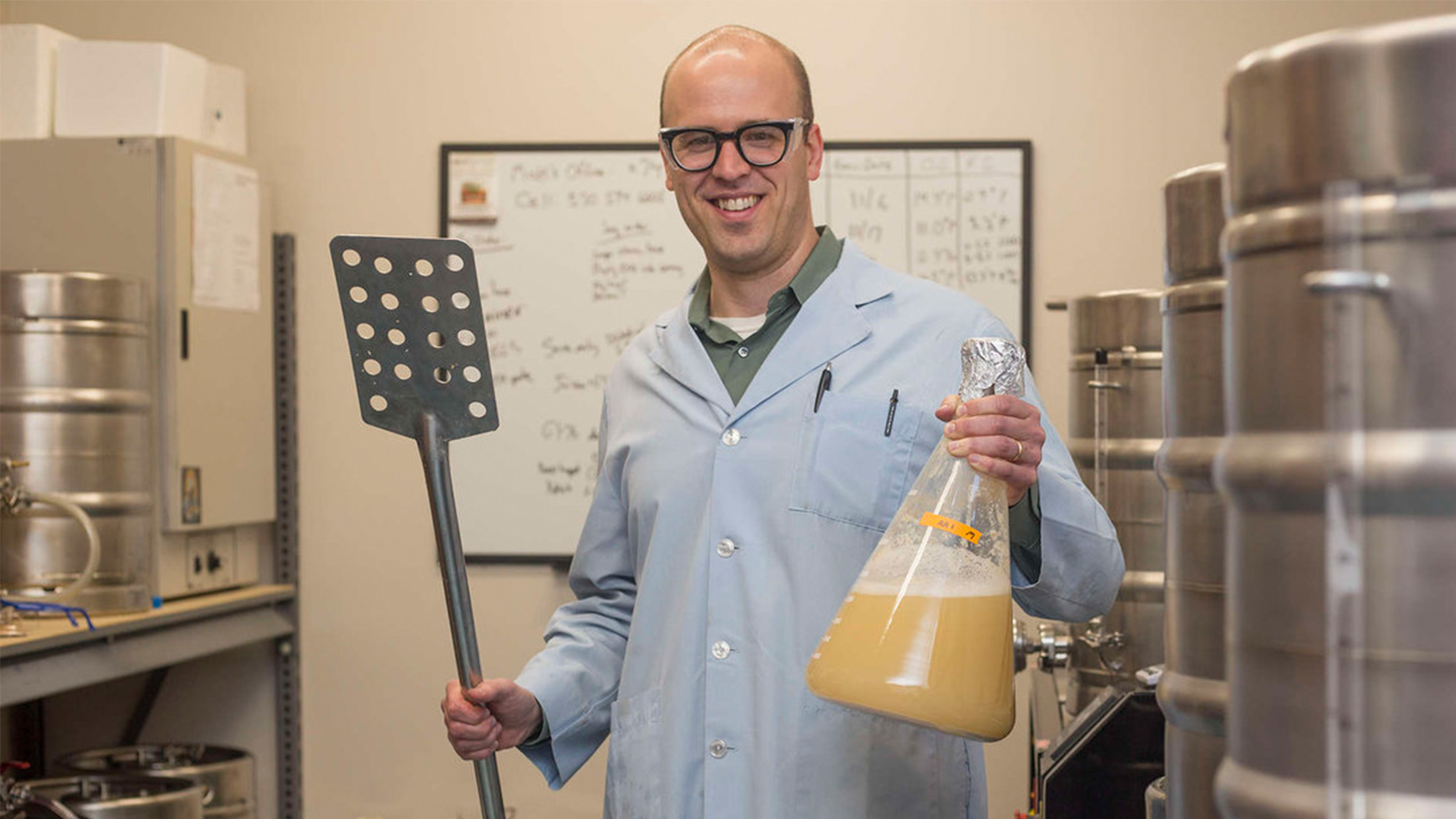 Matthew Farber, PhD, stands in Saint Joseph's pilot brewing lab with a giant flask of yeast.