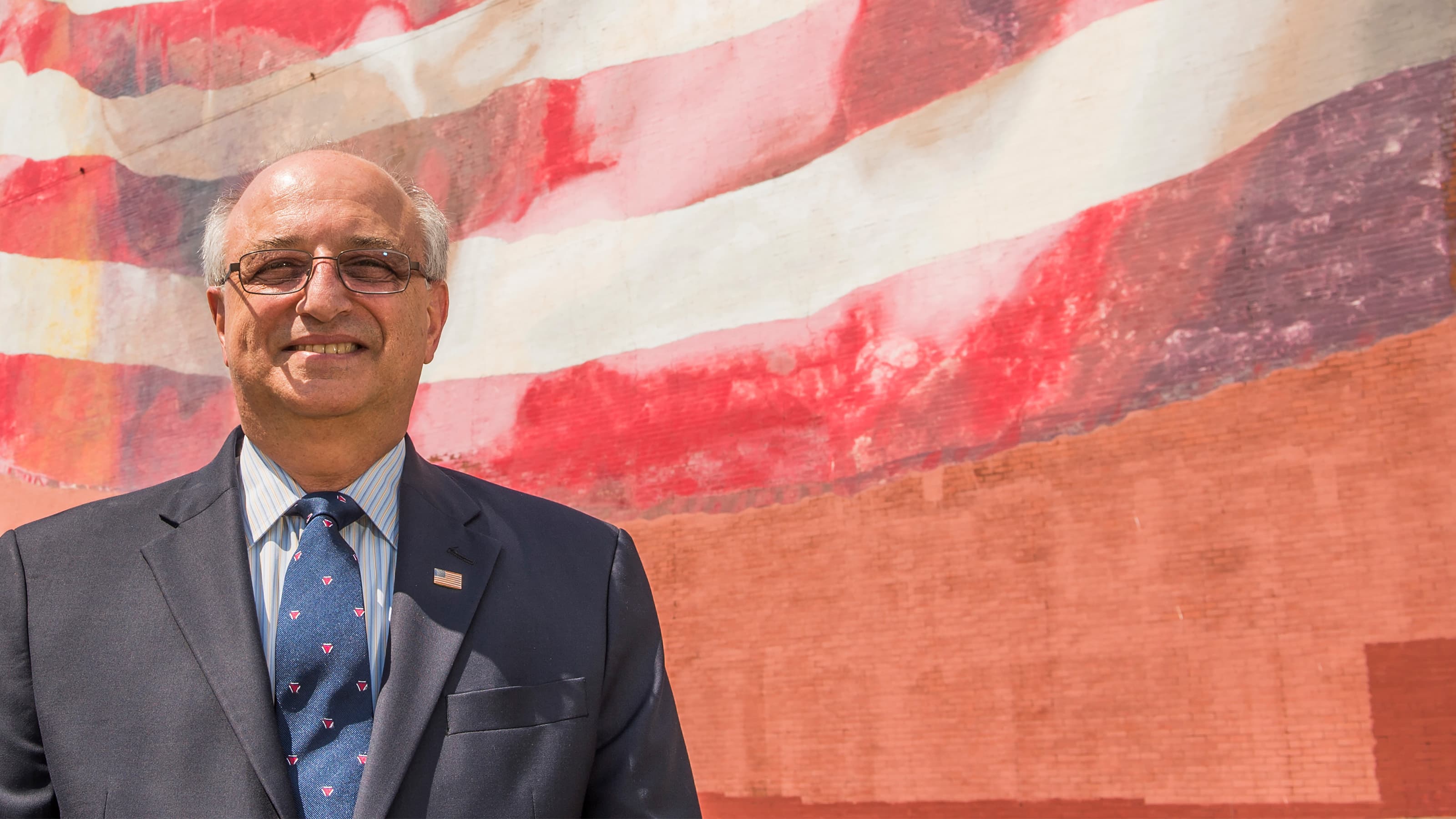 Ralph Galati '70 standing in front of an American flag mural