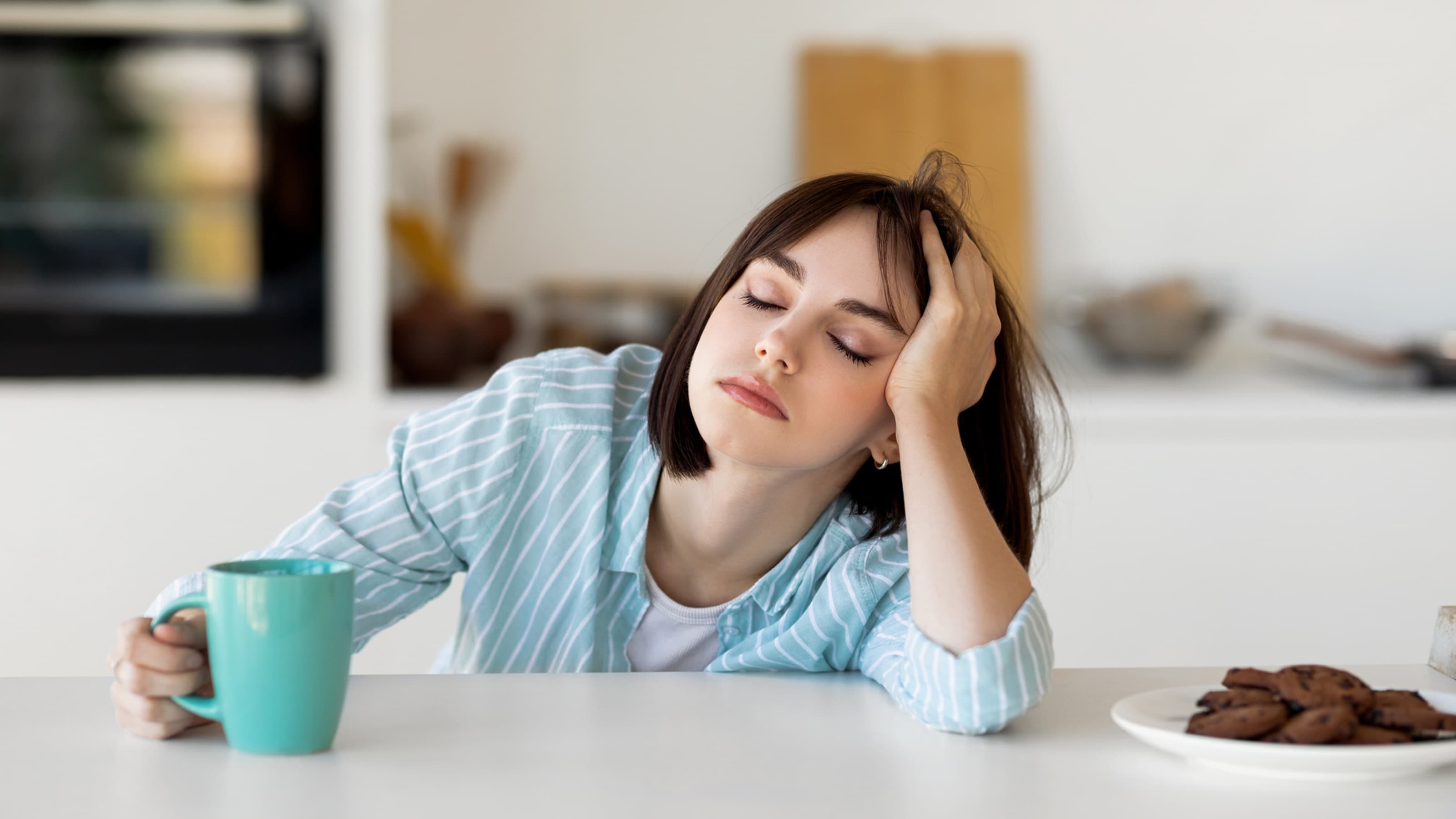 Tired woman leaning on counter drinking coffee