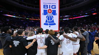 SJU men's basketball team standing in front of the Big 5 flag