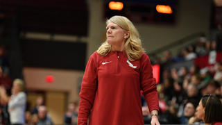 Saint Joseph's coach Cindy Griffin standing on basketball court with audience behind on bleachers