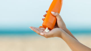 A woman pouring sunscreen into her hand on the beach.