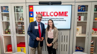 Don DiJulia and Madison Lujan in front of memorabilia wall