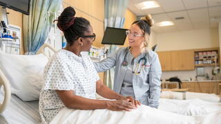Female nurse tending to a female patient on hospital bed 