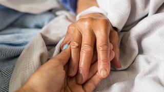 Elderly family member in hospital bed holding female family members hand