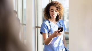 Mid adult female doctor text messages on her smart phone as she walks down the hospital corridor.
