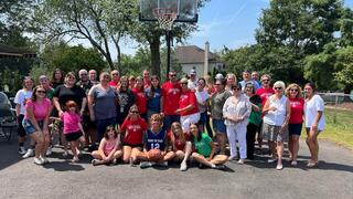 A group of smiling people in front of a driveway basketball net.