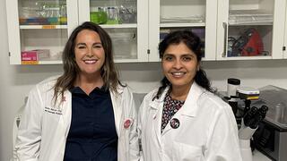 Two female faculty in white lab coats in a science lab