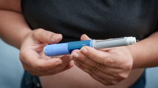 Two hands holding a GLP-1 injector