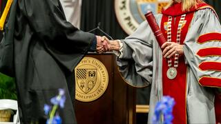 President and student in regalia at graduation shaking hands