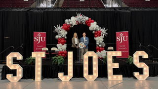 Stefano Billis, BS ’26, and Cheryl A. McConnell, PhD, on stage under a balloon arch with light up St. Joe's letter's in front of them.