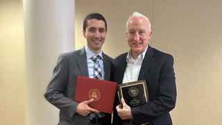 Father Peter Clark and Fredy Abboud, BS ’25 standing together with his degree in hand.