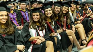 A group of graduates seated in regalia smiling for the camera