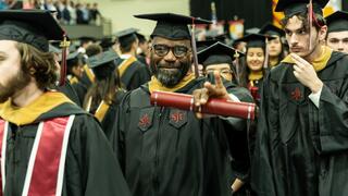 Smiling graduate pointing to camera in regalia