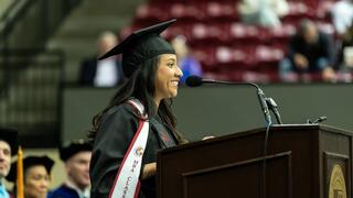 Magaly Urban in regalia speaking at a podium