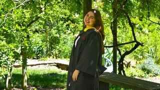 Nicole Bowen in her regalia standing under trees