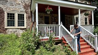Male student paints the stair railing of a stone house