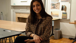 Faith Belcuore sits at a desk in an art studio
