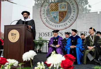 Speaker at podium at Commencement ceremony with faculty seated to the right