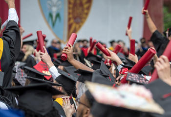 Students in black caps and gowns holding their red diploma scrolls in the air