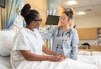Female nurse tending to a female patient on hospital bed 