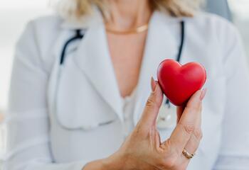 A doctor with a stethoscope holds a small red heart