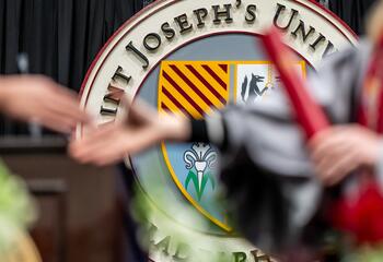 A student receives a diploma in front of the Saint Joseph's University crest.