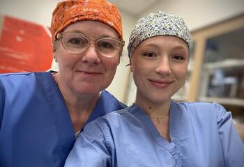 Erica Cabrera, AAS ’26, and Alexandra Gooding, AAS ’25, smile in surgical caps and scrubs
