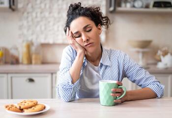 A woman sleeps propped up on her hand at a kitchen table