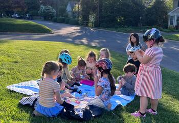 Kids gathered together on a picnic blanket with on a front lawn