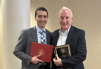 Father Peter Clark and Fredy Abboud, BS ’25 standing together with his degree in hand.