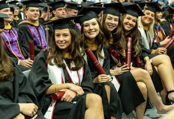 A group of graduates seated in regalia smiling for the camera