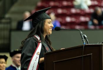 Magaly Urban in regalia speaking at a podium