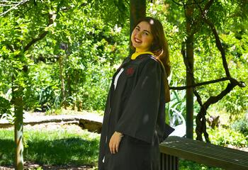 Nicole Bowen in her regalia standing under trees