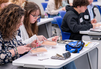 Two high school students practice suturing on a fake arm during their visit to Saint Joseph’s Lancaster location on Feb. 9.